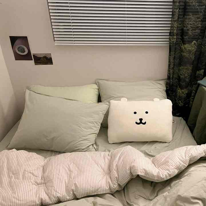 柔らかいグリーンとホワイトの色調の寝室、枕とクマの形のクッションが置かれた落ち着いた空間