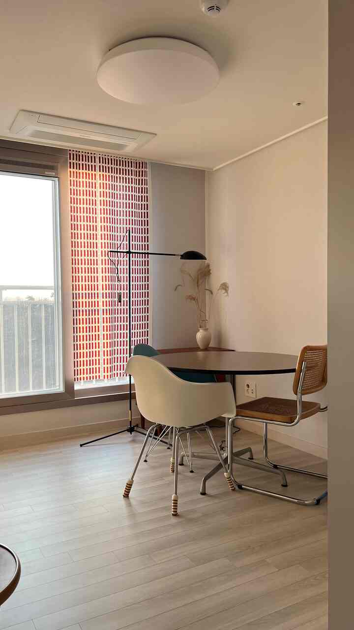 Beige-toned dining room with natural wood floor featuring a round table, Eames chairs, and floor lamp creating a calm cozy space