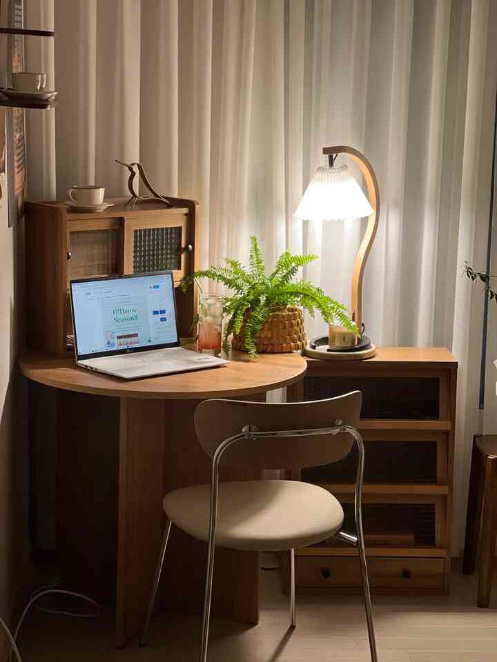Wood tone and white lit small home office space featuring a round wooden table, cabinets, and natural decor with plants