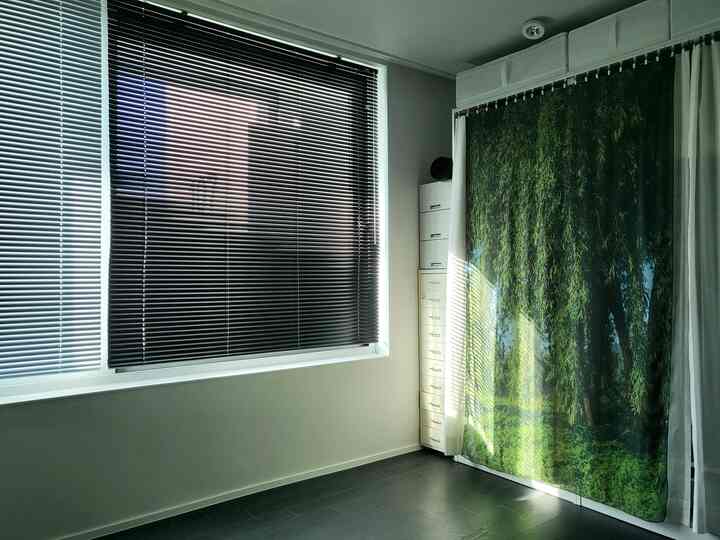 A bright modern walk-in closet featuring black blinds, white walls, and a natural scene fabric curtain