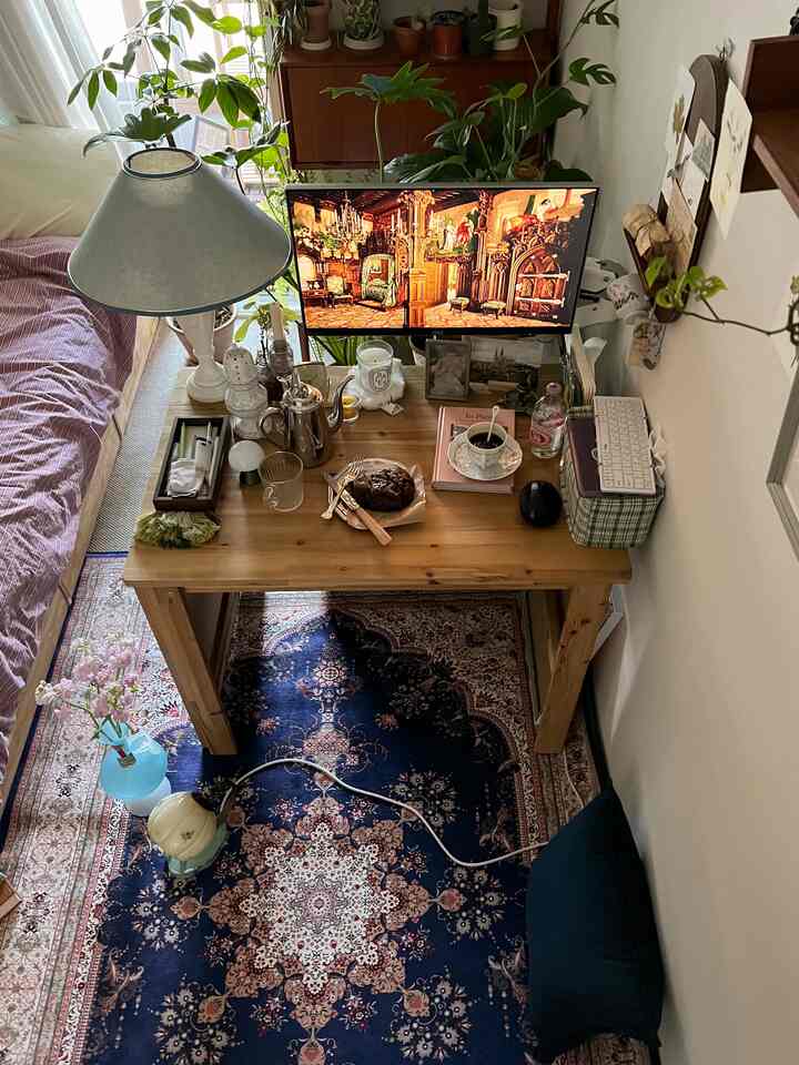 ナチュラルトーンの寝室、木製デスクとペルシャ風ラグ、多数の植物と照明が配置された雰囲気のあるホームオフィス環境