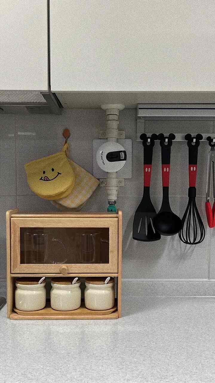 Natural color and yellow toned kitchen featuring kitchen utensils and neat storage cabinet with cozy atmosphere