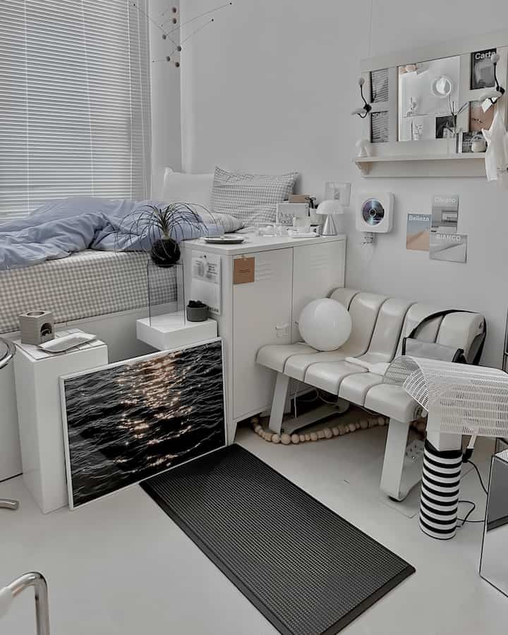 A white and gray toned bedroom featuring a bed with checkered bedding on the left, a bench and small lighting on the right in a clean modern space