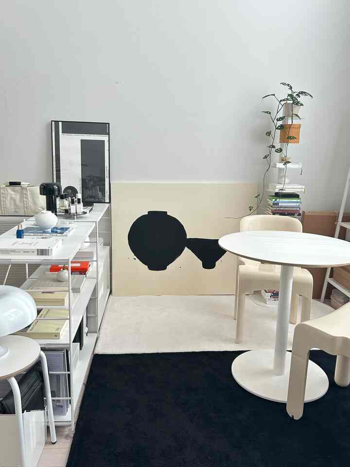 Natural modern small room featuring white and beige tones with a round dining table, chairs, white shelves, and a framed poster creating a home cafe atmosphere