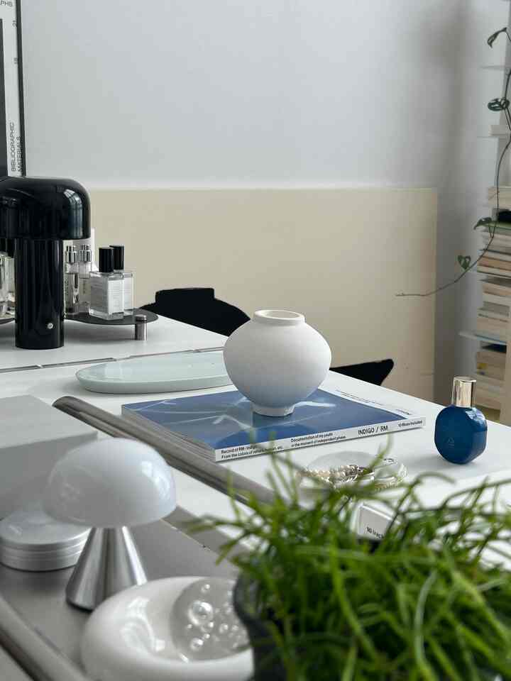 白とネイビーの配色が印象的なテーブル上に丸いオブジェと香水、本が配置されたシンプルでモダンな室内空間