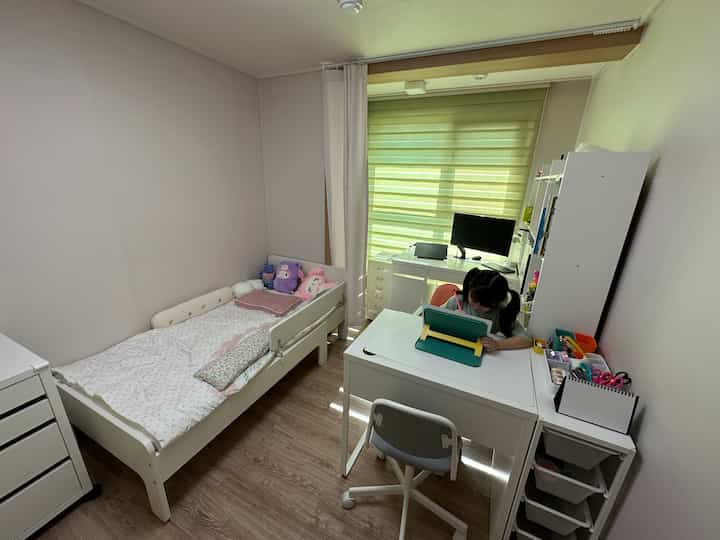 ホワイトとナチュラルトーンの子供部屋、デスクとベッドが配置された清潔で居心地の良い空間