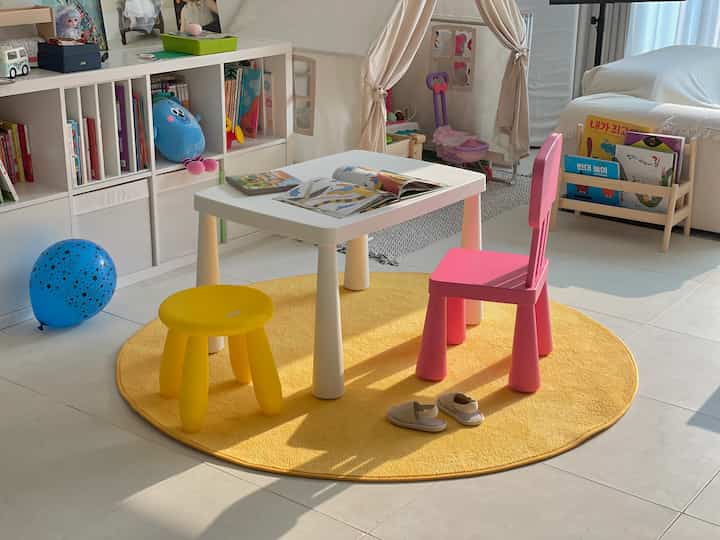 Bright modern kids' room with white tiled floor and yellow round rug, featuring a small white table with pink and yellow child chairs