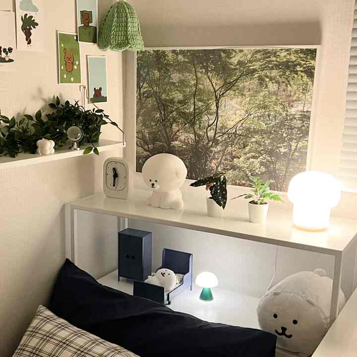 Cozy small bedroom corner in white tones and natural elements with simple shelving housing plants, lamps, and cute plush toys