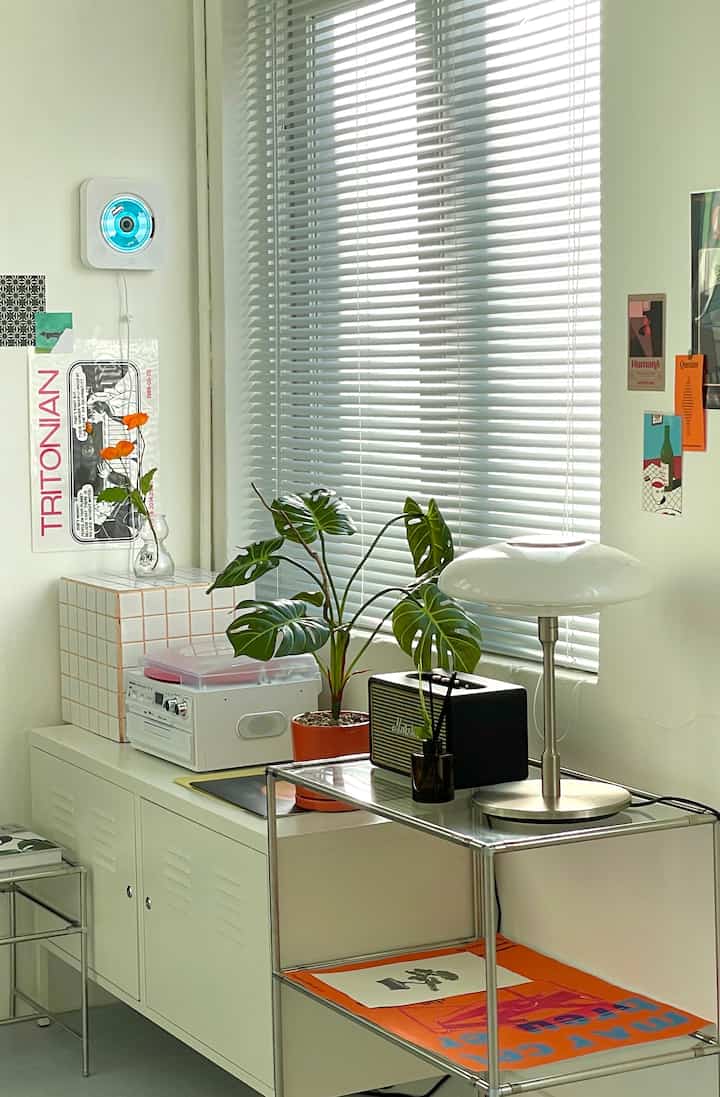 White-toned living space featuring a white cabinet, blinds, monstera plant, and mid-century modern furniture creating a cozy ambiance