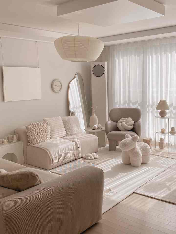 アイボリーとベージュの色調のリビング、ソファとアームチェア、プラッシュスツールが配置された落ち着いた自然な雰囲気のインテリア