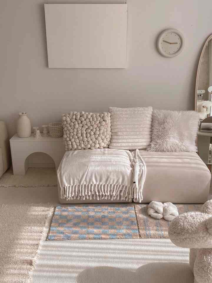 Beige and cream toned living room featuring a sectional sofa with textured cushions, wall clock, and canvas art, creating a warm natural ambiance