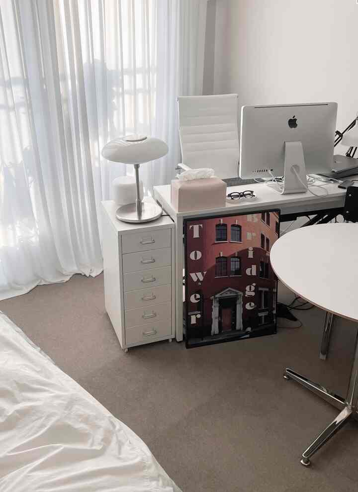 Bright white-toned studio home office featuring desk, dresser, and poster with a clean and minimalist atmosphere
