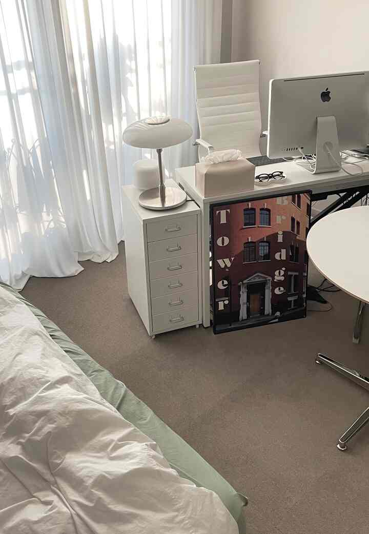 明るいホワイトトーンの寝室とホームオフィス、ベージュのタイルカーペットと明るいカーテンが配置されたミニマルなインテリア