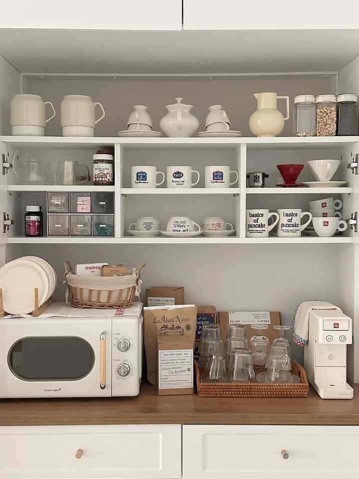 White and wood tone kitchen featuring a coffee machine, oven, and organized cabinets creating a neat home cafe space
