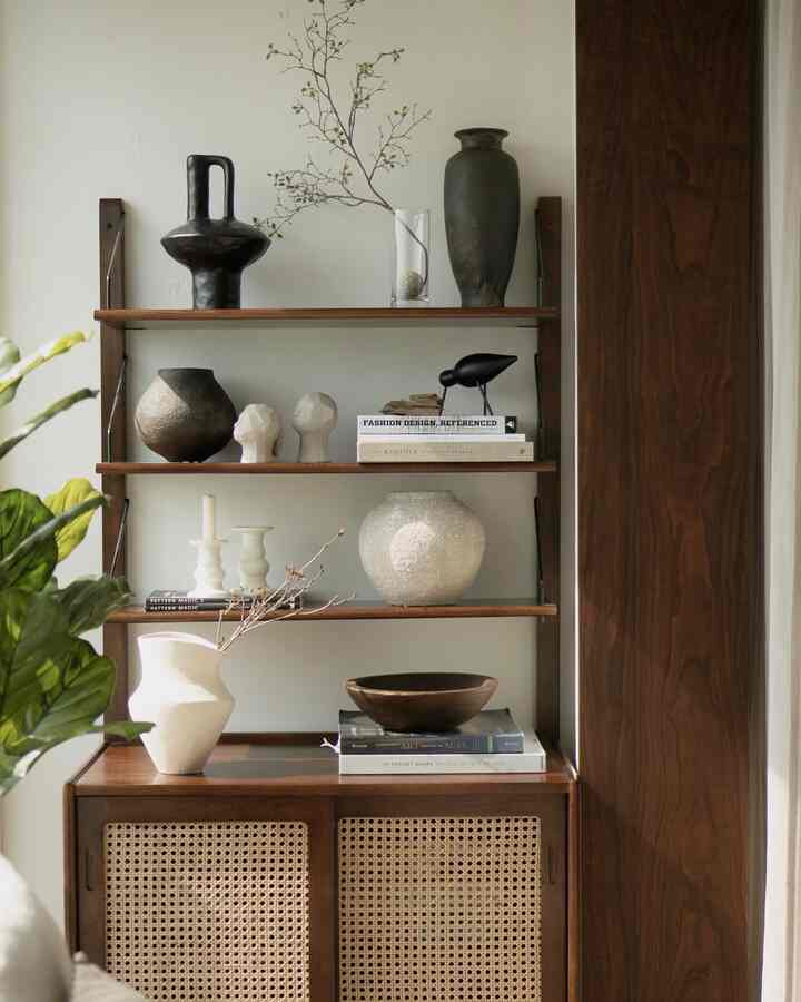 Beige and white toned expanded living room with walnut wood cabinet and wooden shelves displaying diverse objets in a natural setting