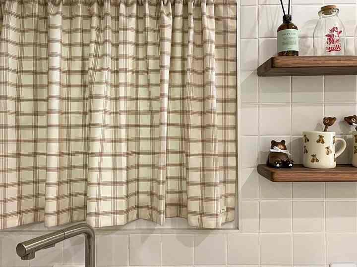 Beige checkered curtains and white tiled wall with wooden shelves displaying cute bear mugs create a cozy kitchen space