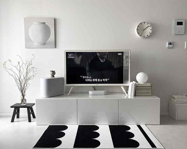 白とグレーのトーンでまとめられたモダンなリビング、中央に光沢のあるテレビ台と白黒パターンのラグが配置されたシンプルな空間