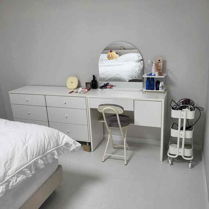 Clean white-toned bedroom with a white dresser, vanity desk, and white bedding arranged in a simple space
