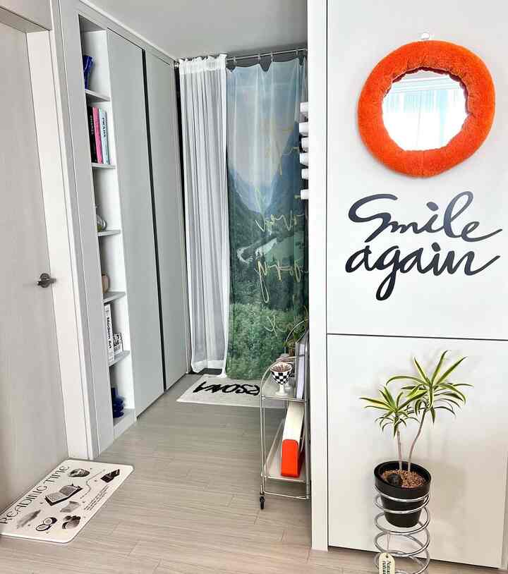 白と緑のトーンの玄関スペース、自然をテーマにしたファブリックポスターと移動式トロリーが配置されたシンプルな雰囲気のインテリア