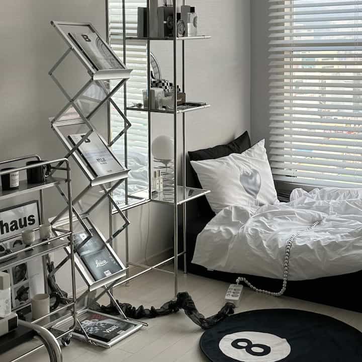 モノトーンとグレーの小さな寝室、白い寝具とブラインド、メタル棚が配置されたミニマルな雰囲気のインテリア