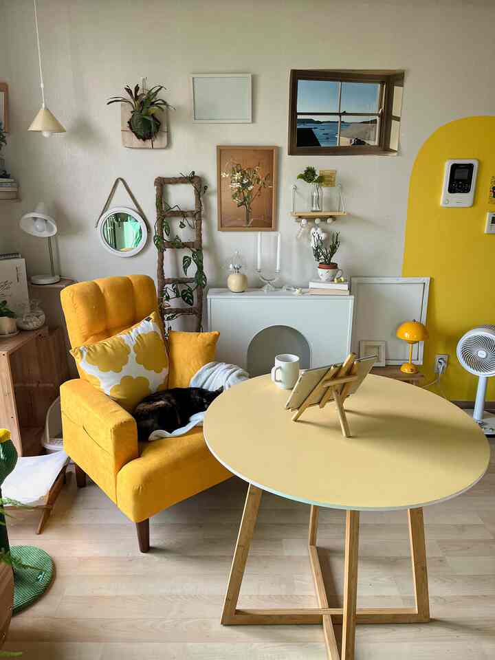 明るい黄色とナチュラルウッドトーンが調和したリビング、黄色の一人掛けリクライナーアームチェアと丸テーブル、ソファには猫が快適にくつろいでいる