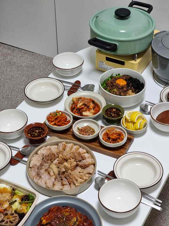 白いテーブルに多様な皿と韓国の引っ越し祝い料理が整然と並べられた様子