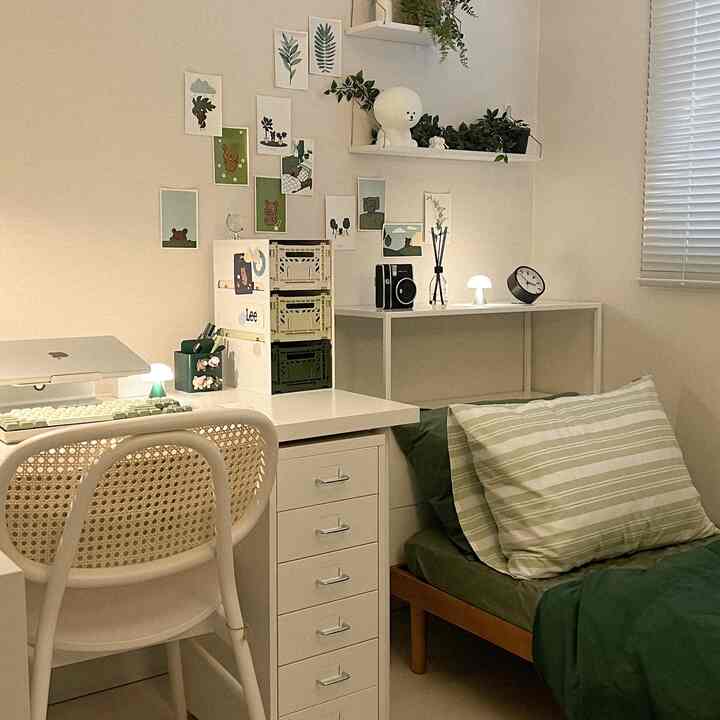 白と緑のトーンの小さなワンルーム寝室、ベッドとデスクが並び、自然な雰囲気のあるインテリア