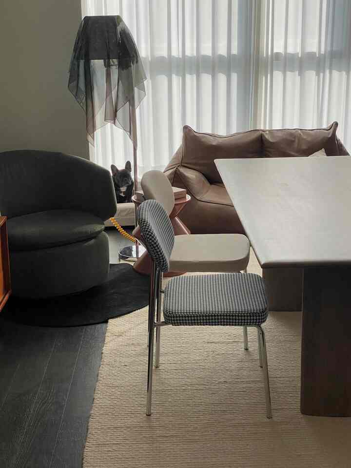 Natural toned living room featuring brown leather sofa, gray armchair, dining table with chairs creating warm and cozy atmosphere