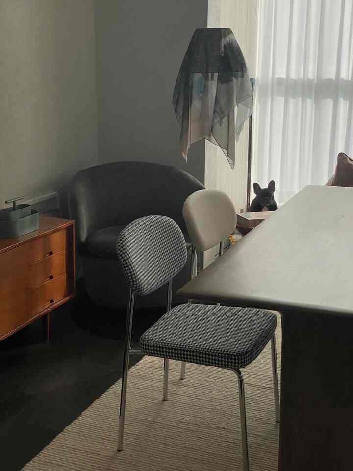 A modern, subdued living room with dark black and gray tones, featuring a wooden side table and armchair, bathed in soft natural light