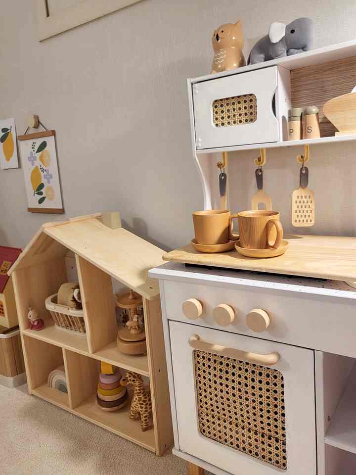 A cozy kids' room corner featuring natural wood tones and white, with wooden toys and a play kitchen set arranged neatly