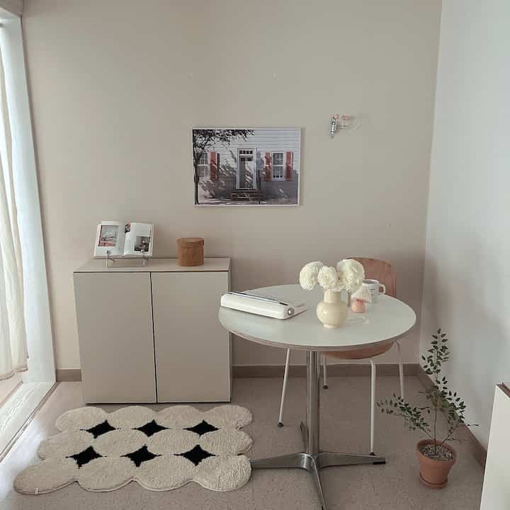 White and natural toned dining room featuring simple dining table and chair, poster, and potted plant creating cozy ambiance