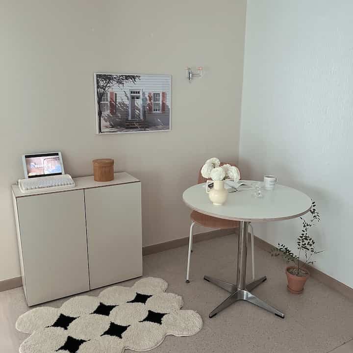Bright white and beige-toned small corner space featuring a round dining table and storage cabinet with a cozy atmosphere