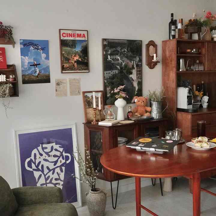 Wood tone and red-hued living room cum home office featuring wooden table, decorative objets, and framed posters with cozy cafe-style ambiance