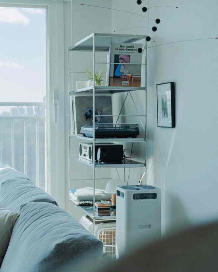 White-toned living room featuring a blue-gray sofa and metal storage shelving, creating a modern and clean space