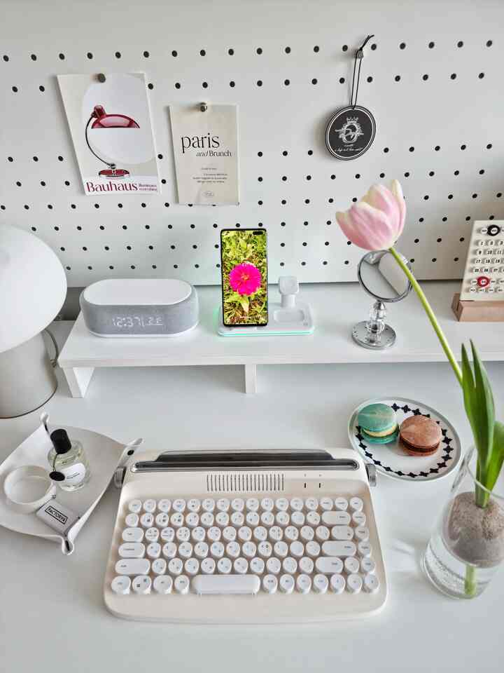 White-toned home office desk featuring vintage keyboard and vase with flower in neat, simple space