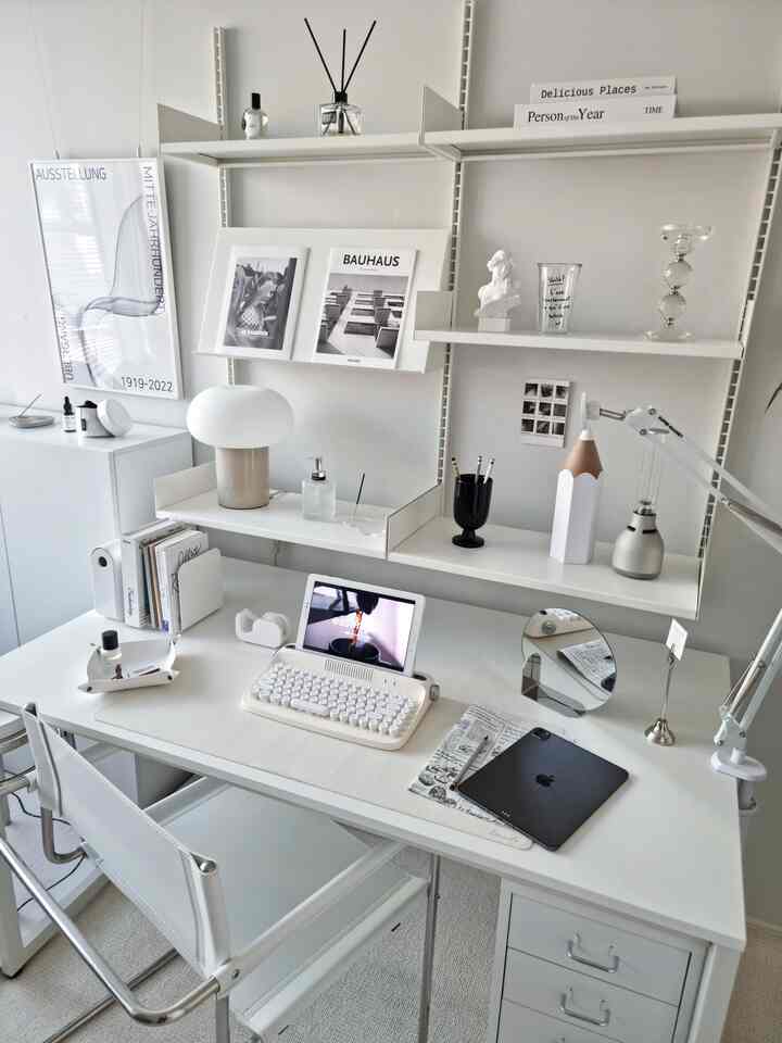 White-toned home office space featuring a tidy desk, modern lighting, and framed artwork in a simple desk interior
