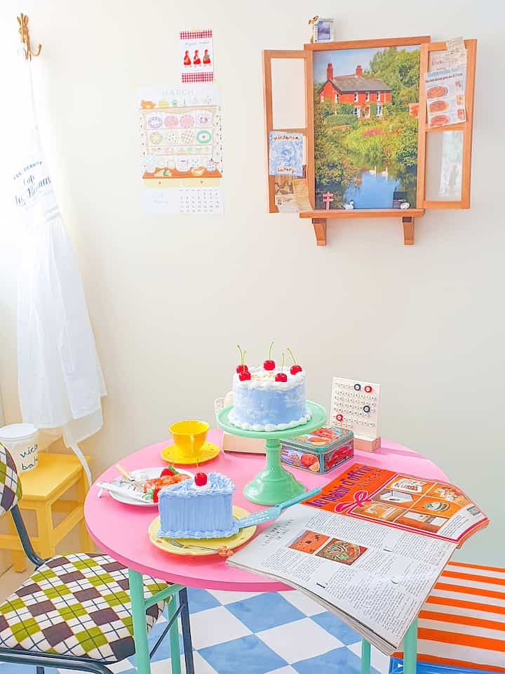 パステル調のかわいらしいカフェ風インテリア、ピンクの丸テーブルにケーキと小物が置かれたミッドセンチュリーモダンのスタジオ空間