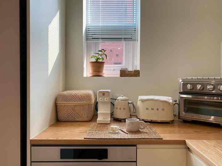 ナチュラルカラーのキッチン、窓辺に植物が置かれ、コーヒーマシンとススメグの家電が木製カウンターに整然と配置された雰囲気のあるインテリア