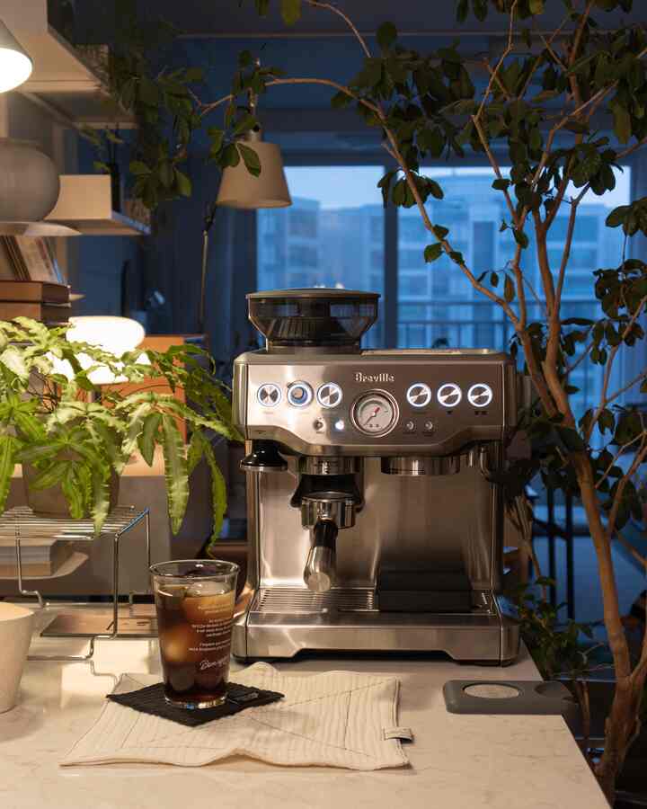 暖かい照明とシルバーのコーヒーマシン、緑の植物が配置された自然な雰囲気のホームカフェキッチン