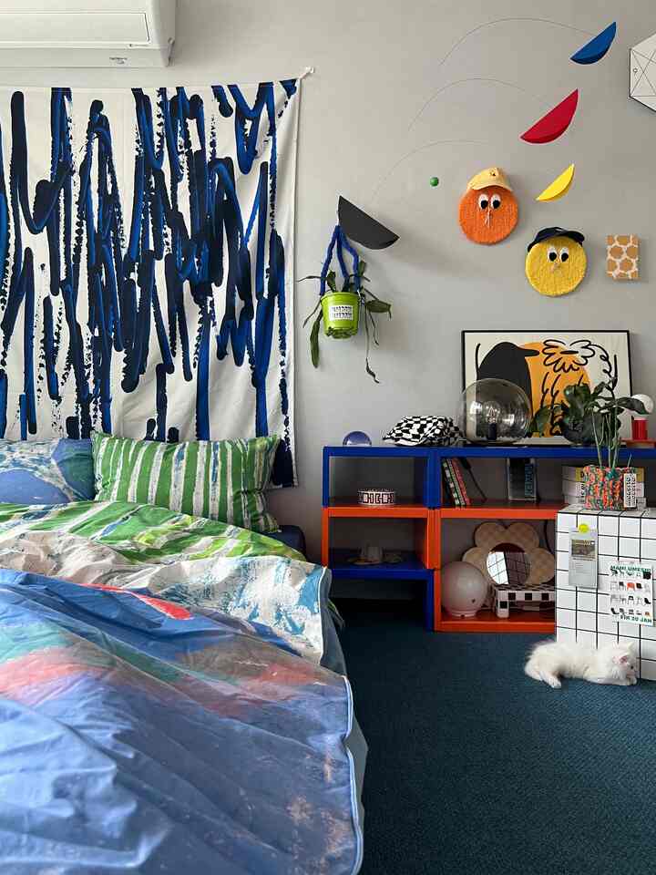 鮮やかなブルーとグリーンの色調の寝室、カラフルな収納棚と壁のアートが配置された個性的な空間