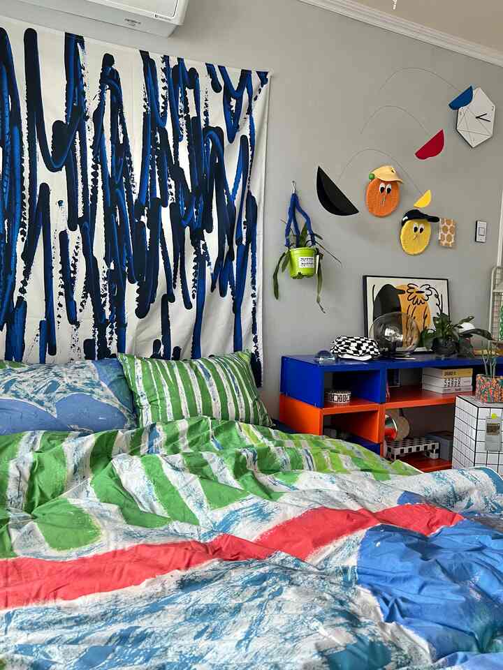 Colorful bedroom space featuring a central bed, framed artwork, and wall-mounted mobile and plant stand in a modern Nordic style interior