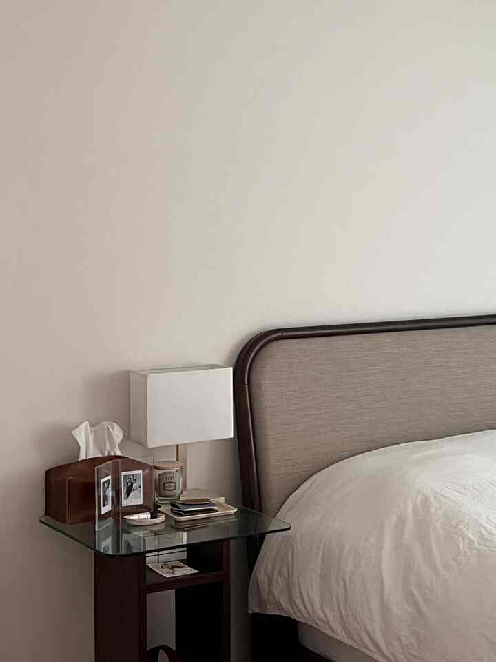 白と茶色のトーンの寝室、ヘッドボード付きベッドとガラストップのサイドテーブルが配置された雰囲気のあるヴィンテージスタイルの空間