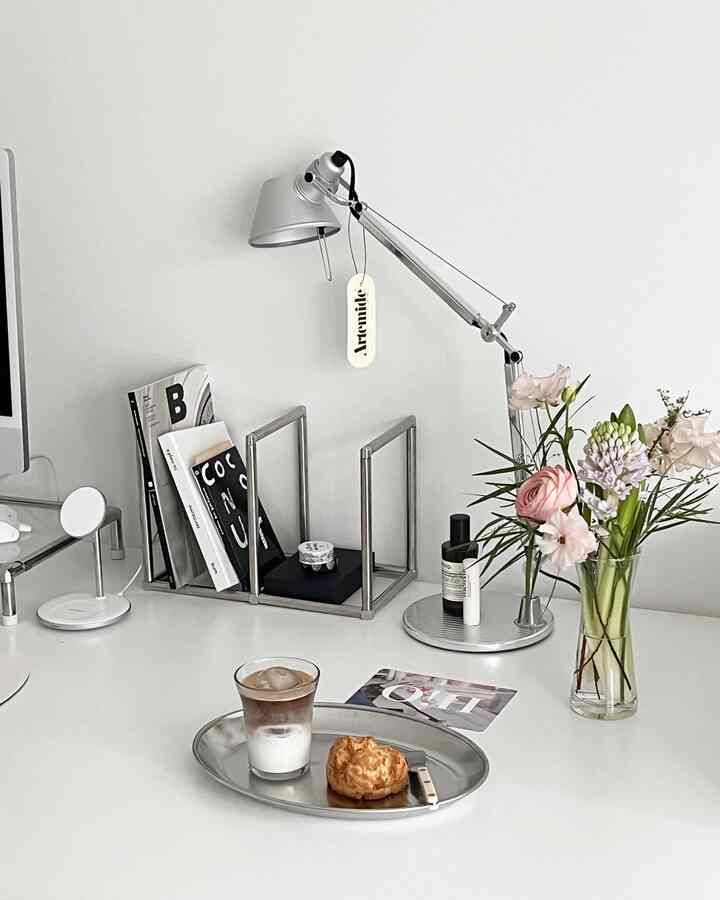 Minimal style workspace with white tones featuring a desk lamp, flower vase, and home cafe elements on a clean desk