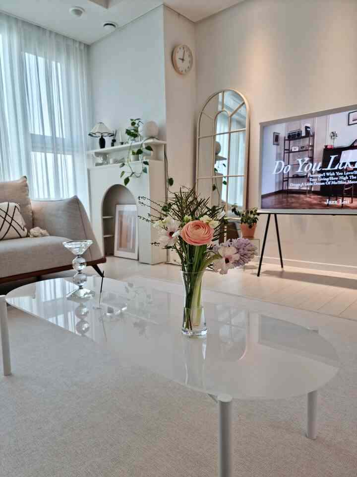Bright white-toned living room featuring a central white coffee table with a vase and candlestick, showcasing a simple modern design