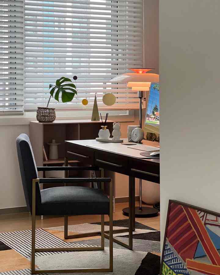 Study with white blinds and wood-tone flooring, featuring dark desk and armchair as central elements in a calm home office