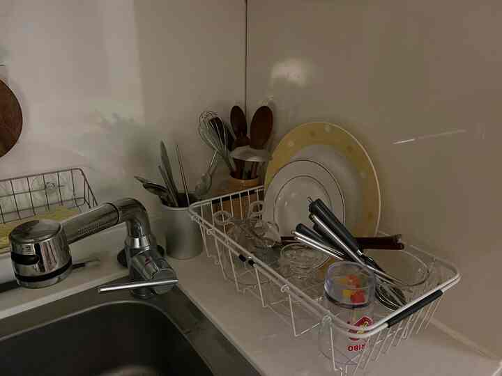 White tone kitchen space featuring a sink, dish rack with cutlery sets and kitchen utensils arranged neatly