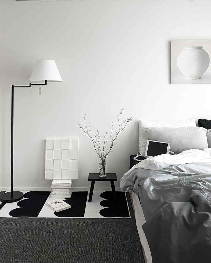 A white and black toned bedroom featuring a modern bed, rug, and floor lamp creating a simple and calm space