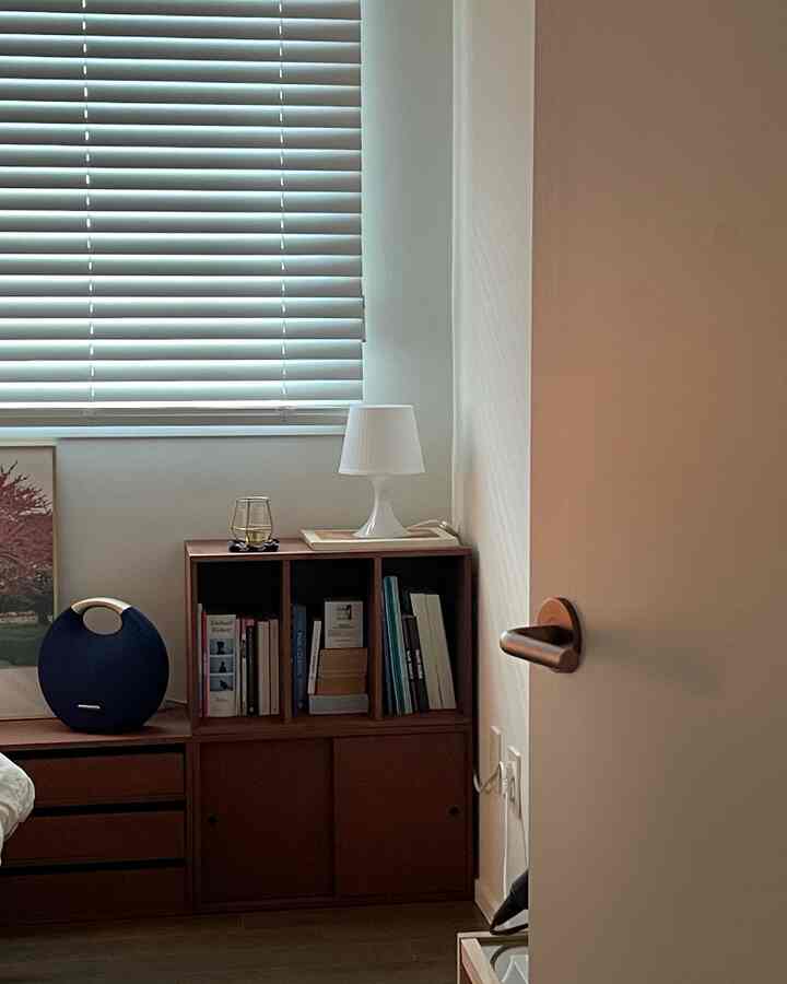 A cozy bedroom with white walls and wood tone cabinet, featuring soft lighting and arranged books