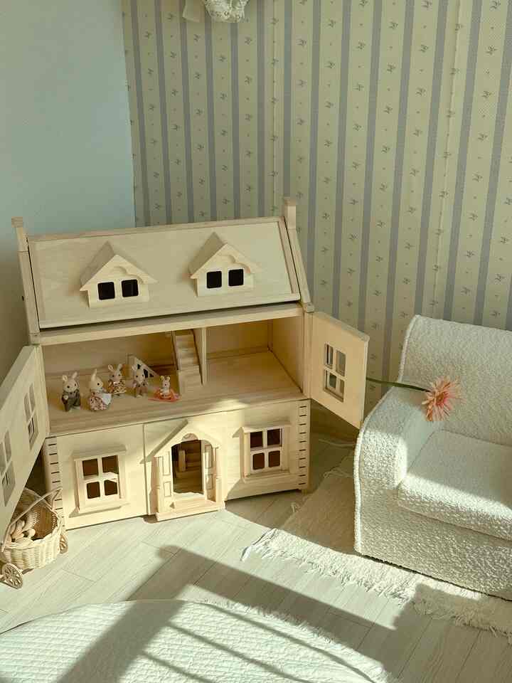 Natural tones kids' room corner featuring wooden dollhouse, ivory textured armchair, and rug in a cozy setting