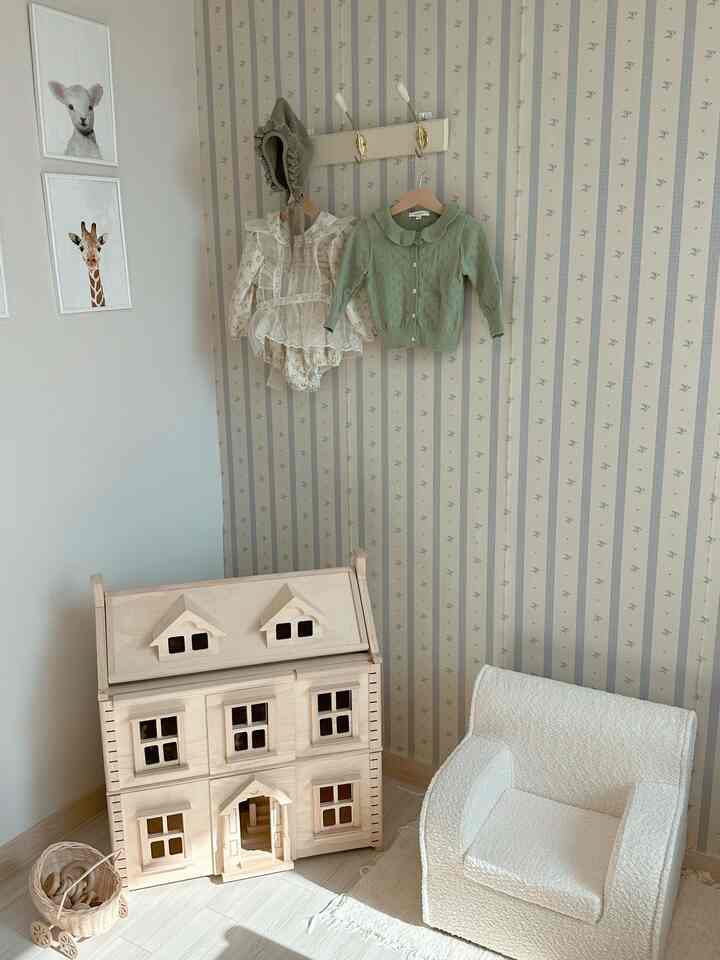 白と木目調の調和のとれた子供部屋、木製のドールハウスとベビー服が配置された温かみのある自然なインテリア